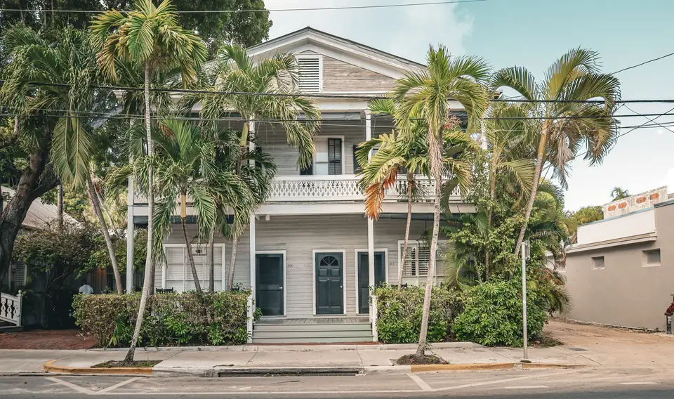 Two-story home with porches behind palm trees